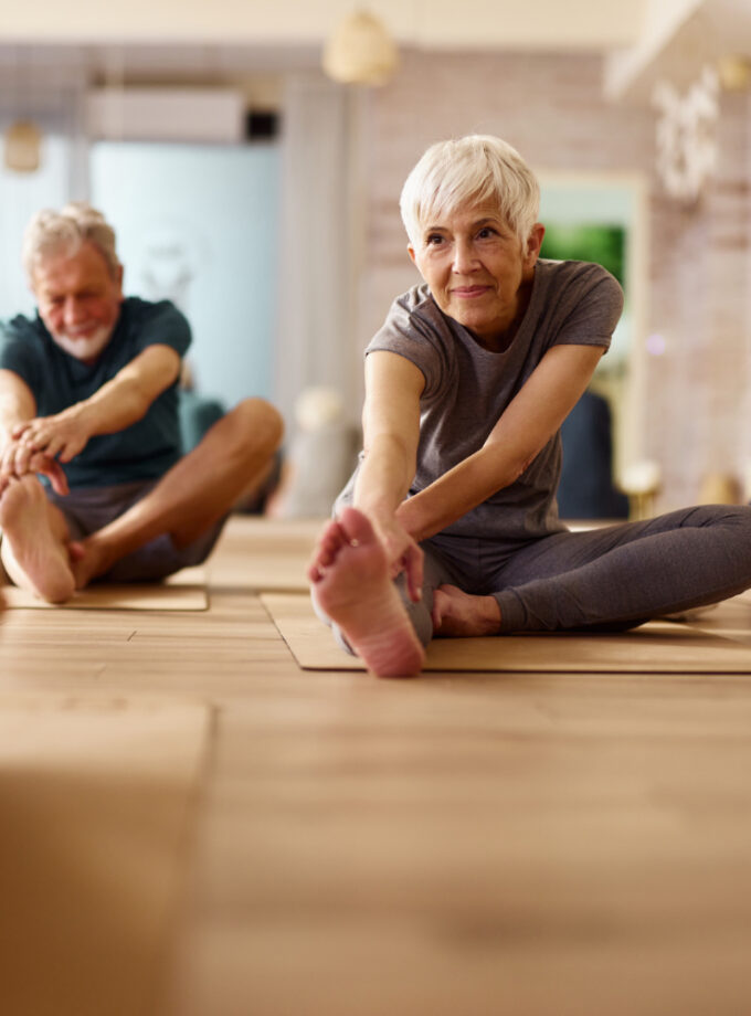 A group of seniors wondered: hypnosis is it real? Perform stretching exercises. One senior woman is achieving more restful sleep and has more energy from hypnosis and sleep. She is happily exercising with her coach and Yoga class mates, after using hypnosis for weight loss and exercise.