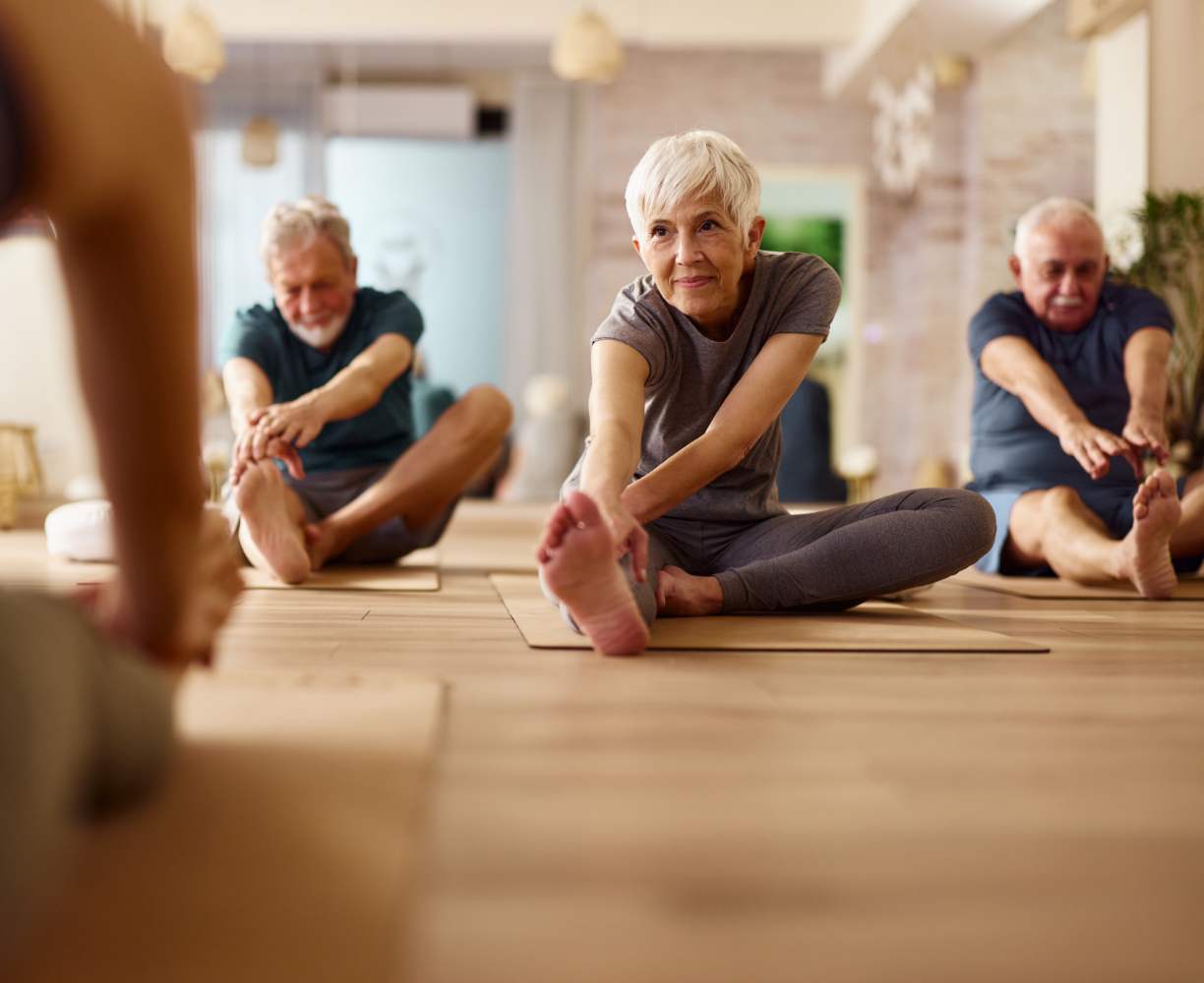 A group of seniors wondered: hypnosis is it real? Perform stretching exercises. One senior woman is achieving more restful sleep and has more energy from hypnosis and sleep. She is happily exercising with her coach and Yoga class mates, after using hypnosis for weight loss and exercise.