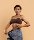 A fit African American woman smiling confidently. Used self hypnosis. She is showing her now over sized jeans, after successful fat loss hypnosis to remove belly fat.